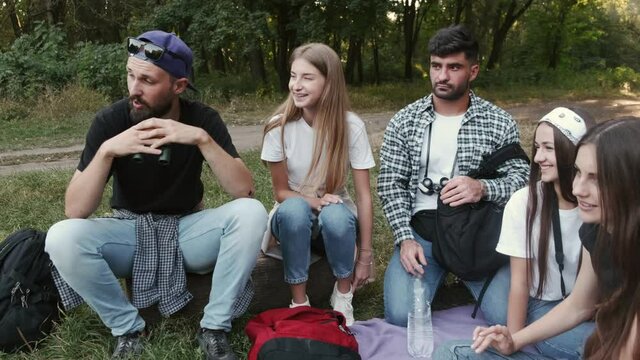 Camping and hiking. Group of young students going hiking in the forest. The people are having a break, sitting in a circle they are talking and laughing. Friendship goals.