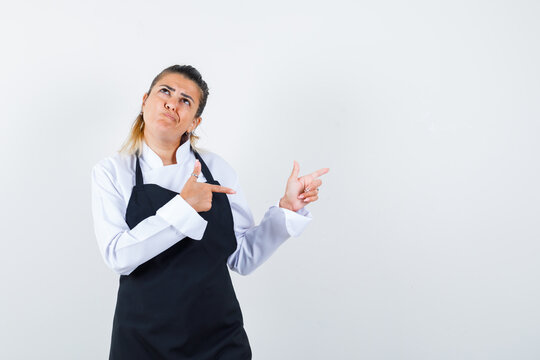  Female Chef In Uniform, Apron Pointing To The Right Side And Looking Hesitant , Front View.