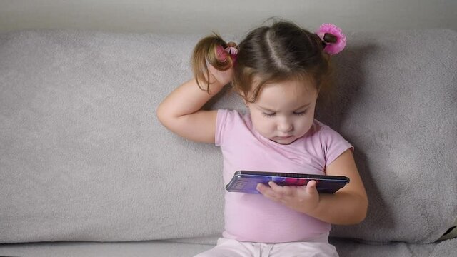 A little girl with ponytails on her hair is watching cartoons on a tablet