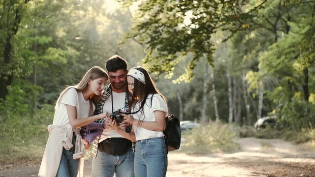Photosession in nature.Tourism. A young man is showing photos on camera to his friends. The girls are laughing. Taking photos.