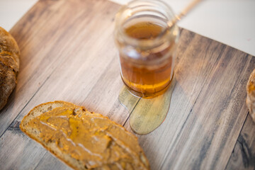 Honey jar and a slice of bread with peanut butter on wooden table