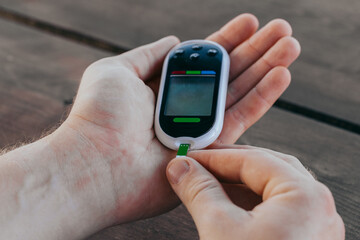 medicine, diabetes, glycemia, healthcare and people concept - man checking blood sugar with glucometer and test strip at home.