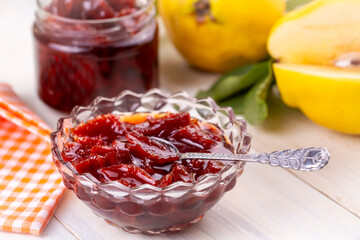 Homemade quince jam in a glass jar on an old wooden background. Fresh quince fruits and leaves and quince jam.
