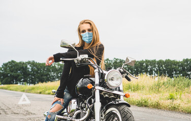 Fototapeta na wymiar Beautiful girl biker in a medical face mask sitting on the motorcycle. Lifestyle during quarantine concept.