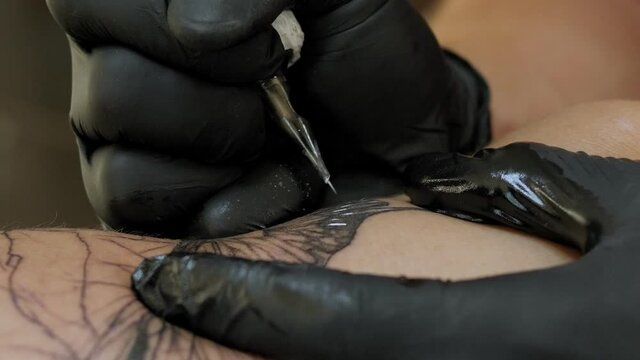 Needle tattoo machines inject a black ink into the skin of a woman. Tattoo art on body.