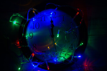 A minute before the new year. Clock on a dark background with New Year's lights.