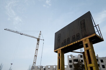 Old rusty scoreboard. Construction site with tall crane equipment. Industrial background.