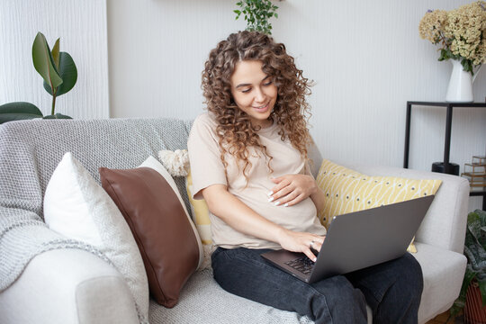 Charming pregnant girl holding hand on tummy, using the free Internet and a laptop browsing sites with toys for future baby. Pregnancy, motherhood and technology concept.