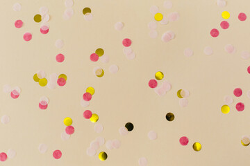 Pink, gold confetti on beige paper background. Festive holiday backdrop. Birthday congratulations. Valentines Day. Flat lay, top view, copy space.
