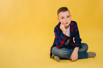 A pensive nine-year-old boy in a shirt in a cage sits on a bright yellow background.