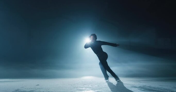 Cinematic shot of young male figure skater with headphones is performing training choreography on ice rink before start of a competition. Concept of technology, love and passion for sports and music