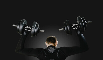 A man performs exercises using weights on a dark, black background. The concept of sports and...