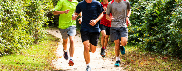 Four boys running together on a dirt path surrounded by bushes