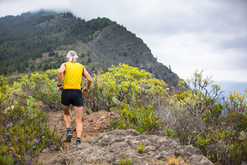 Old man in yellow t-shirt running on the trail to the mountains of canary island la palma