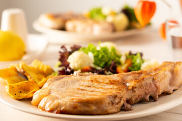 Fried pork entrecote on the bone with stewed pumpkin pieces and salad in a plate close up, green salad with cauliflower and napa cabbage, bell pepper and spices