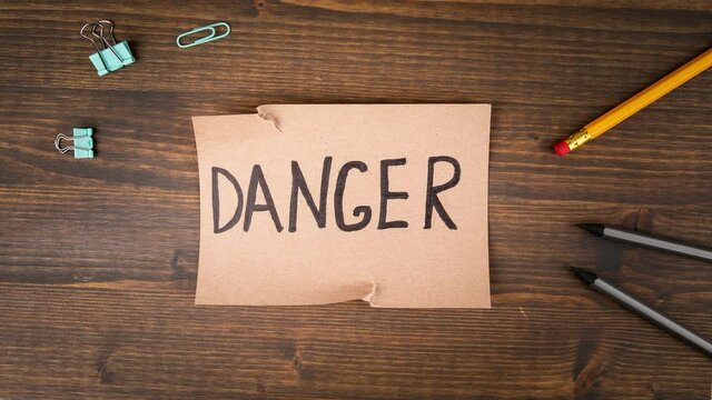 Danger. Torn cardboard with an inscription on a wooden background