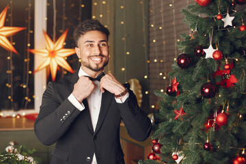 Handsome man near Christmass tree. Gentelman in a black suit.