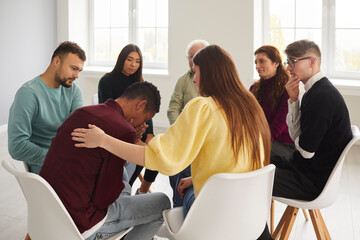 Diverse people supporting and comforting crying young man in group therapy session