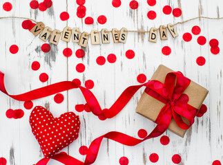 Valentines day gift box with a red ribbon and heart shape on white wooden background, inscription from wooden letters.