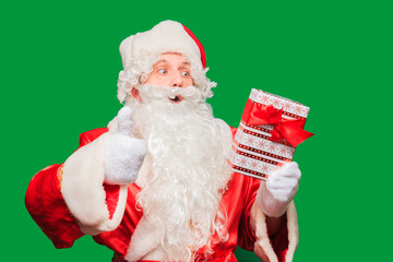 Santa Claus holding nicely wrapped Christmas present isolated on green colored background.