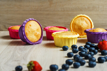Muffins in multi-colored paper tins and blueberries on a light wooden background. Sweet pastries. Homemade baking. Sweets for the holiday. Freshly baked cupcakes on a wooden background.