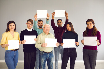 Group of different people standing together, holding white sheets of paper and looking at camera