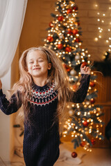 Merry Christmas concept. The child is dancing merrily near the Christmas tree at home. Merry Christmas celebration at home.