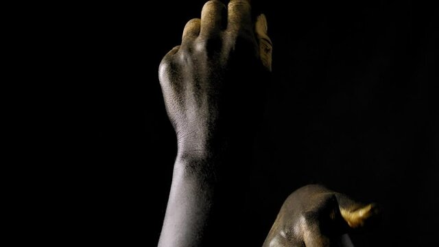 Close-up of a young woman's hands in black and gold paint on skin on a black background.