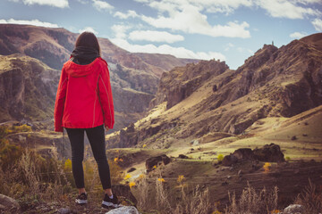 Naklejka premium Woman stands on the edge and admires dramaic landsacape of caucasus in Vardzia. Georgia. Solo freedom and travel blogging.
