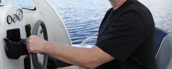 Man's hand in t-shirt holding floating motor boat steering wheel, cabin watercraft interior...