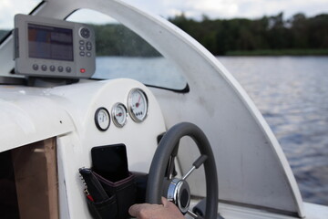 Man's hand on floating motor boat steering wheel, cabin watercraft interior dashboard with control...