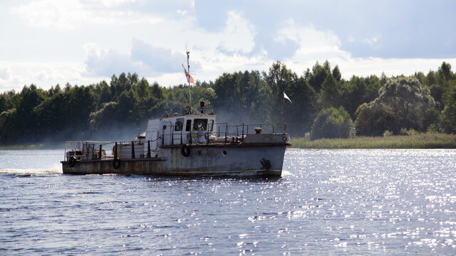One old Soviet mini tug boat with inboard motor diesel smoke slowly floating on calm river water on forest and cloudy sky background at Sunny summer day, outdoor recreation