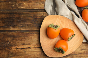 Tasty ripe persimmons on wooden table, flat lay. Space for text