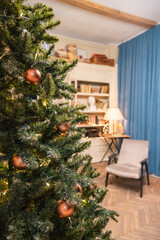 In the foreground in focus is a Christmas tree decorated with Christmas balls. In the background is a place to read, a chair and a table near the bookcase. Cozy and calm atmosphere