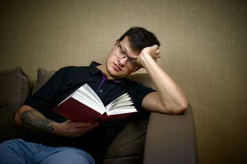 Obraz premium A man is reading a book sitting on the sofa. Thoughtful man reading a book