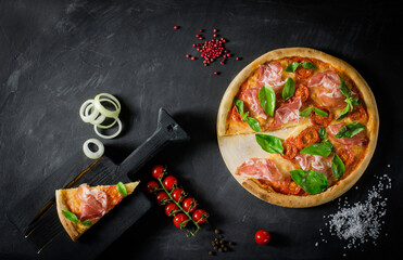 Top view to Italian pizza with prosciutto, tomato, mozzarella and ingridients on a black background