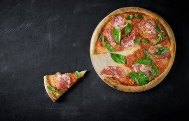 Top view to Italian pizza with prosciutto, tomato, mozzarella, basil on a black background