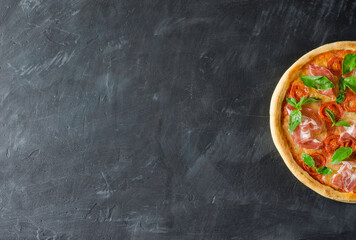 Top view to Italian pizza with prosciutto, tomato, mozzarella on a black board with copy space