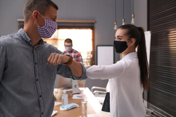 Obraz premium Coworkers with protective masks making elbow bump in office. Informal greeting during COVID-19 pandemic