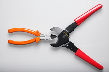Big red wire cutter for huge size of copper cables placed close to small cutter with orange handle. Electrical engineering tools composition isolated on white background.