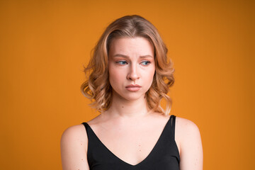 A portrait of a moody Caucasian girl isolated on orange background. She's dissapointed and sad, looking sideways and pouting lips