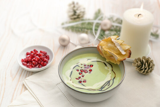 Apple and peas soup with pomegranate seeds and baked camembert bread, appetizer course from a festive holiday menu on a white wooden table with candle and Christmas decoration, copy space
