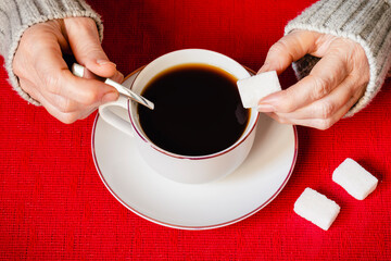 Una mano poniendo un terrón de azúcar en una taza de café, sobre un mantel rojo