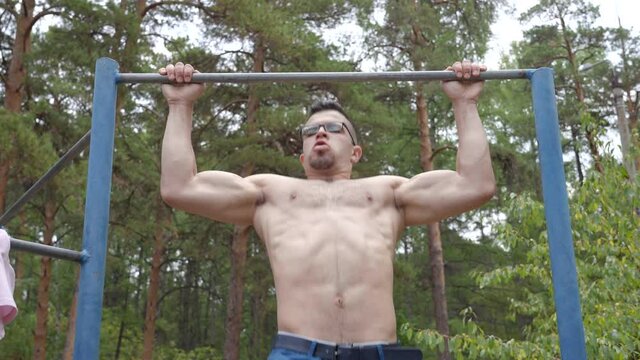 Guy bodybuilder of middle eastern appearance pulls himself up on a horizontal bar in the forest.
