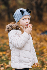 A beautiful little girl, a child in a jacket of preschool age, indulges, smokes a cigarette, imitating adults. Autumn funny portrait, photography.