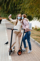 Young beautiful girls in masks ride in the Park on an electric scooter on a warm autumn day and take selfies. Walk in the Park.