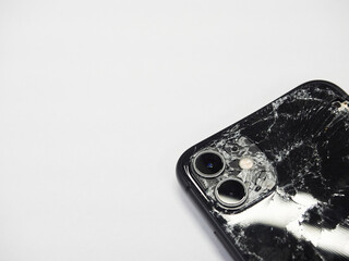 Los Angeles, California, USA - 01 December 2020: (Top view) The back of the black iPhone 11 has broken glass on white background. Modern smartphone with damaged back glass.