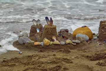 Sand castle made with colorful rocks and shells next to ocean waves.