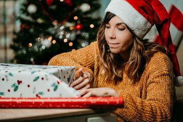 .Pretty young woman in a santa hat wrapping christmas presents at home. Christmas time