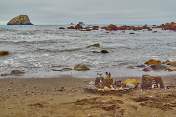 Sand castle made with colorful rocks and shells next to rocky ocean shoreline.